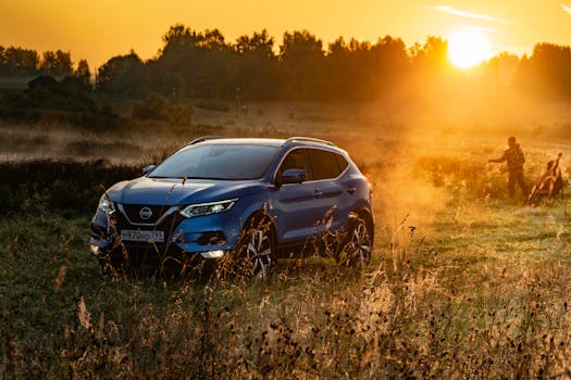 Blue SUV in a rural field at sunset with a man and child in the background.